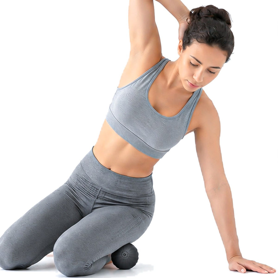 Woman kneeling with the RECOVERO TRIGGER POINT ROLL trigger point massage ball under her thigh